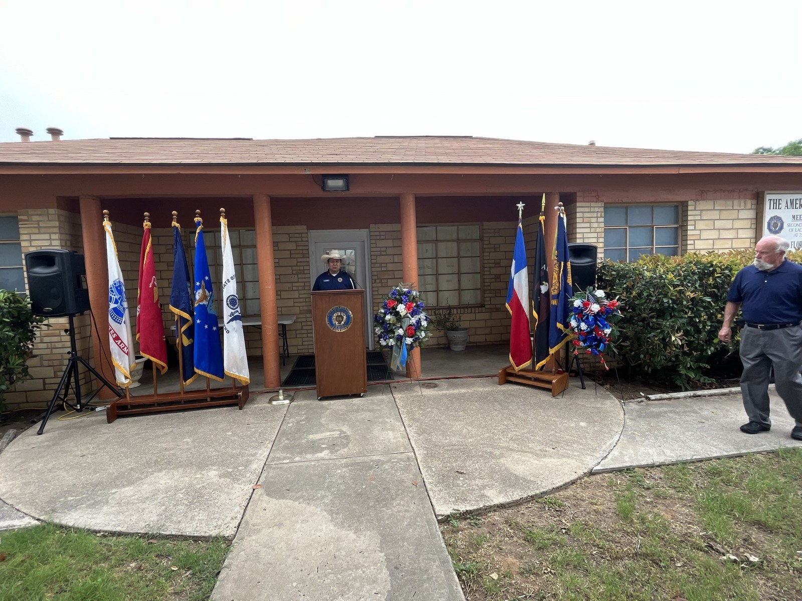 Outdoor ceremony at American Legion Post with podium and service flags